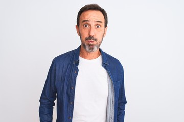 Middle age handsome man wearing blue denim shirt standing over isolated white background puffing cheeks with funny face. Mouth inflated with air, crazy expression.