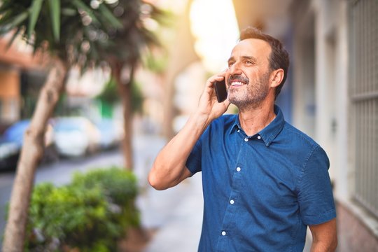 Middle age handsome businessman standing on the street talking on the smartphone smiling