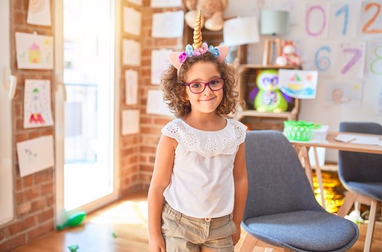 Beautiful toddler wearing glasses and unicorn diadem standing and smiling at kindergarten