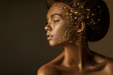 Fashion art portrait of model girl with holiday golden shiny professional makeup. beaty woman with gold metallic body and hair on dark background. Gold glowing skin. copy space