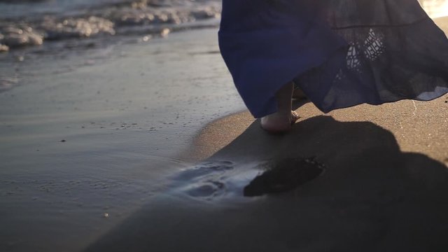 woman in a skirt walks along the coastline in windy weather at sunset, skirt develops in the wind, slow motion