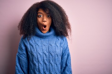 Young beautiful african american woman with afro hair wearing winter sweater over pink background afraid and shocked with surprise expression, fear and excited face.