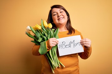 Beautiful plus size woman celebrating mothers day holding best mom message and tulips with a happy face standing and smiling with a confident smile showing teeth