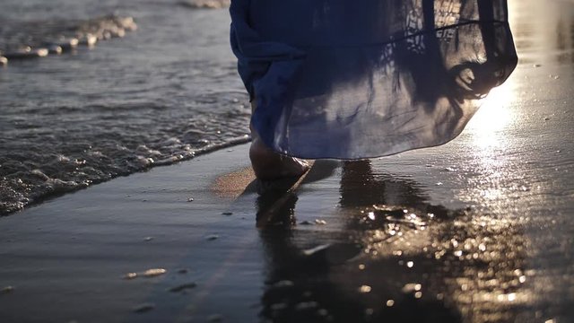 woman in a skirt walks along the coastline in windy weather at sunset, skirt develops in the wind, slow motion
