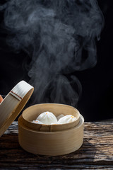 Steam and smoke of hot chinese steamed bun in traditional bamboo steamer on dark...