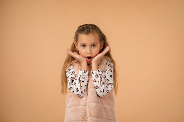 happy surprised beautiful little child girl in sweater looking to camera on beige background. Human emotions and facial expression