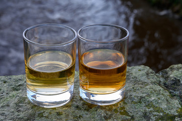Scotch single malts or blended whisky spirits in glasses with water of river Spey on background,...