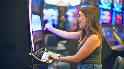 Young beautiful woman smiling happy and confident. Sitting with smile on face playing slot machine at casino