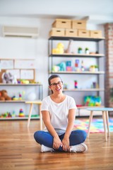 Young beautiful teacher wearing glasses sitting at kindergarten