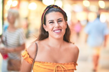 Young beautiful girl smiling happy and confident walking at the town street, standing with a smile on face around night lights bokeh