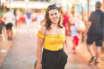 Young beautiful girl smiling happy and confident walking at the town street, standing with a smile on face around night lights bokeh