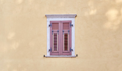 Fototapeta premium Italian windows on the yellow sandy color wall facade with closed new modern wooden red-brown color shutters
