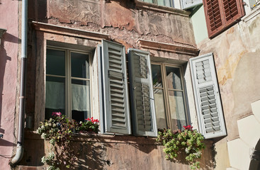 Two old italian windows on the very old wall facade with old wooden white color shutters