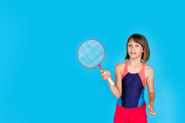 Young teenager girl jumping and playing badminton on blue background