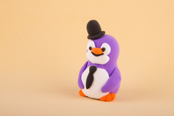 Cute toy penguin made of colored polymer, light clay staying on beige background