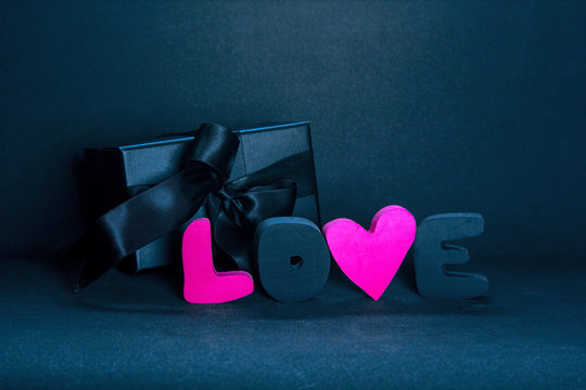 Black gift box and red letters LOVE on dark background, copy space. Valentine's day, birthday romantic concept, greeting card.