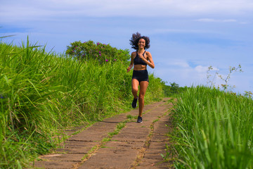 happy female runner training on countryside road - young attractive and fit jogger woman doing running workout outdoors at beautiful track in healthy lifestyle and sport