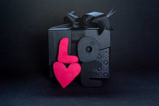 Black gift box and red letters LOVE on dark background, copy space. Valentine's day, birthday romantic concept, greeting card.