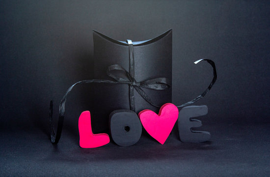 Black gift box and red letters LOVE on dark background, copy space. Valentine's day, birthday romantic concept, greeting card.