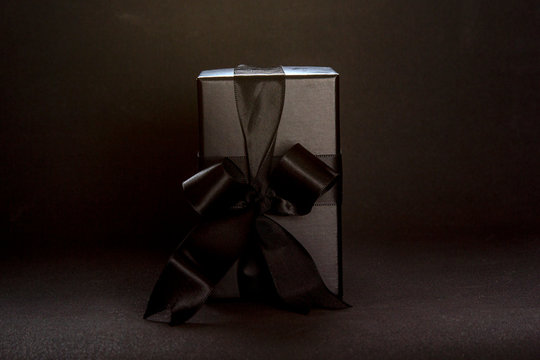 Black creative composition with gift box, black ribbon bow on dark background, copy space. Valentine's day, birthday romantic concept, greeting card.