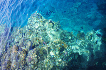 Coral reef in a bright blue sea from above with sun glare on the surface of the water