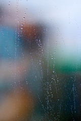 Raindrops on the window glass in front of the city out of focus. Abstract urban background.