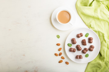 Chocolate candies with almonds and a cup of coffee on a white wooden background. top view, copy space.