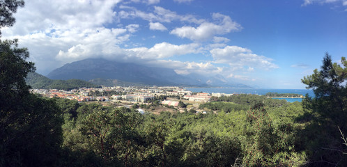 Fototapeta na wymiar Panoramic view from observing place point to Kemer city in Antalya region surrounded by high mountains and blue calm Mediterranean sea on bright sunny day