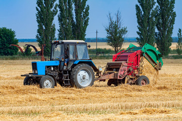 Obraz premium tractor makes big straw roll on yellow field at summer day