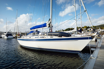 Yachts and boats moored to a pier at sunset. White sloop rigged yacht close-up. Rhu marina, Firth...