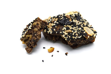 Homemade bread and bakery brownie, cake bitten and crumbs topped with groundnuts raisins sun flower seeds white and black sesame seeds on a white background.