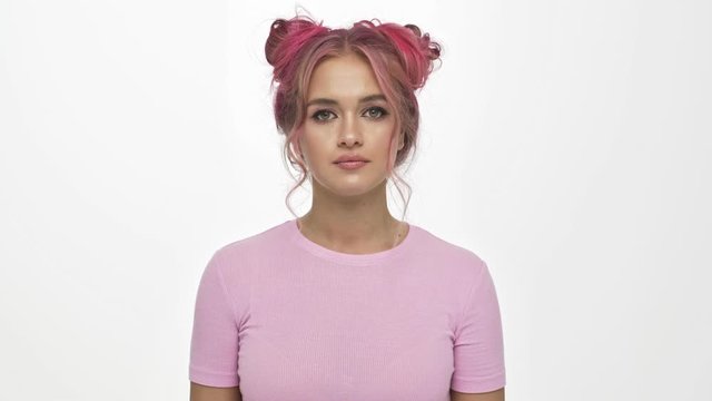 An exhausted young woman with the colored pink hairstyle is doing kill gesture isolated over white background