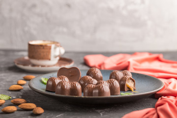 Chocolate caramel candies with almonds and a cup of coffee on a black concrete background. side view, copy space.
