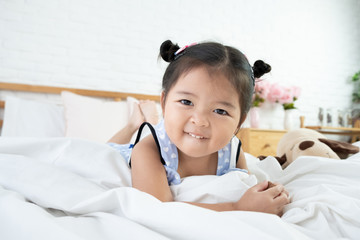 Adorable asian toddler girl 3 years old lie on her stomach in bed feeling happy with smiling face