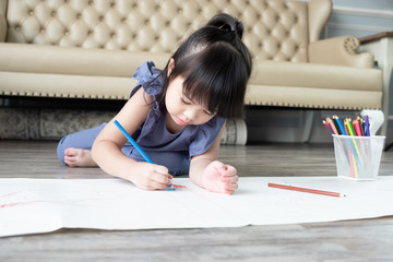 Beautiful Asian child girl lying and drawing with color pencils at home