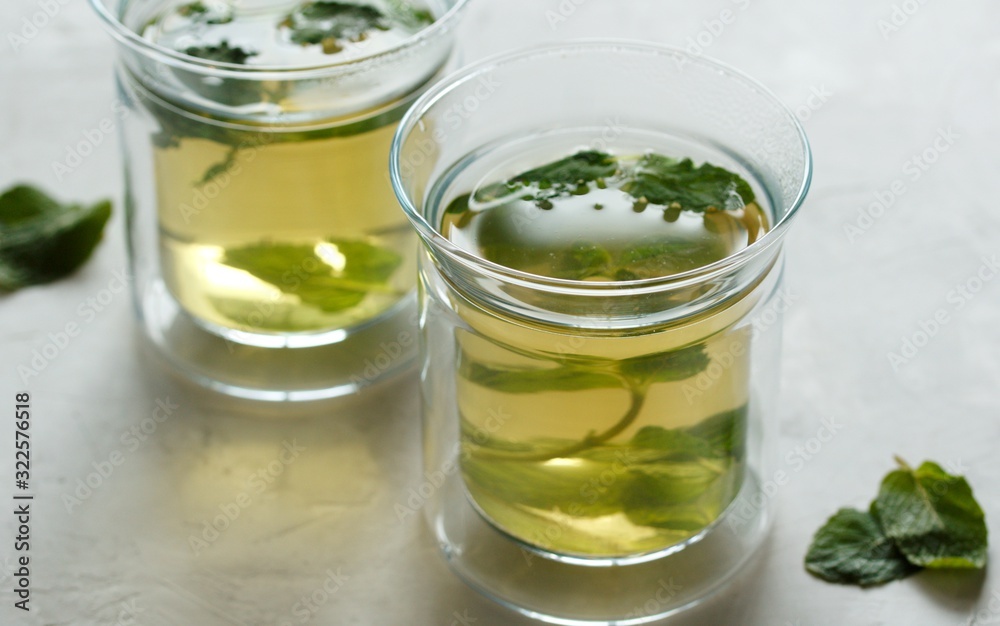 Wall mural Two glass cups with green tea with mint on a light gray table