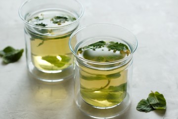 Two glass cups with green tea with mint on a light gray table