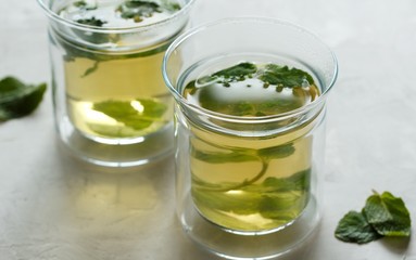 Two glass cups with green tea with mint on a light gray table