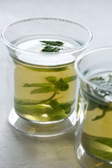 Two glass cups with green tea with mint on a light gray table