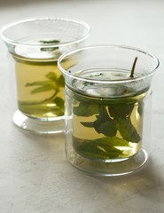 Two glass cups with green tea with mint on a light gray table