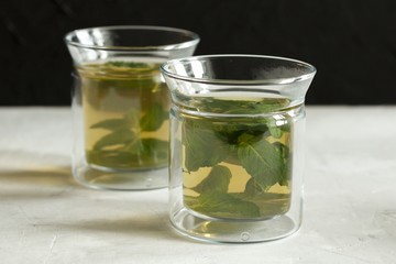 Two glass cups with green tea with mint on a light gray table and on a black background