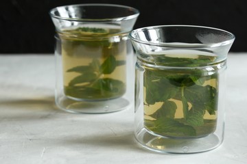 Two glass cups with green tea with mint on a light gray table and on a black background