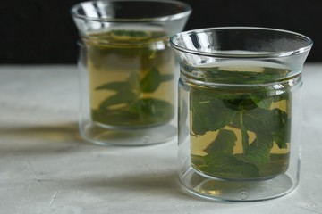 Two glass cups with green tea with mint on a light gray table and on a black background