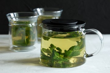 Two glass cups with green tea with mint on a light gray table