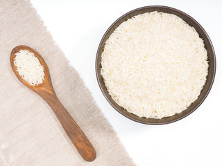 Indian long grain Basmati rise in wooden spoon diagonally and ceramic bowl on white and beige fabric background