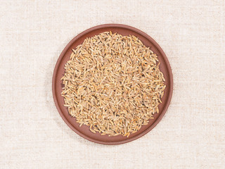 Cumin (jeera) in clay plate on beige fabric background