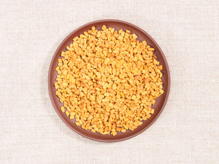 Fenugreek in clay plate on beige fabric background