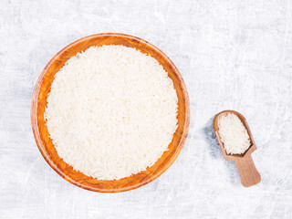 Indian long grain Basmati rice in brown wooden bowl and scoop on white concrete background