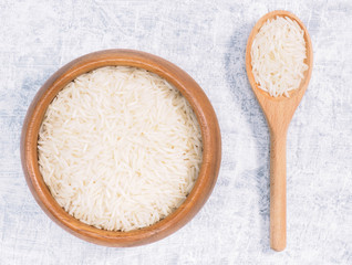 Indian long grain Basmati rice in brown wooden bowl and spoon on white concrete background