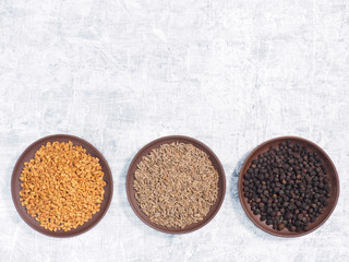 Spice fenugreek, cumin (jeera), black pepper in clay plate on white concrete background